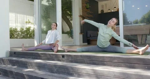 Two women performing side bends and splits on mats on deck outside sliding doors Video stock 340972813