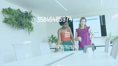 Two women pointing at tablet and leaning over papers, numeric overlays guiding Stock Footage 335316829