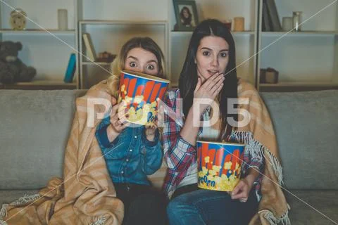 The two women with a popcorn watch a horror movie on the sofa Stock Photos