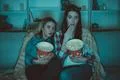 The two women with a popcorn watch a horror movie on the sofa Photo
