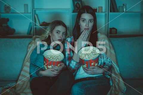 The two women with a popcorn watch a horror movie on the sofa Stock Photos