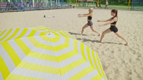 Two women practice lunges on sandy beach, surrounded by vibrant colors Video stock 315860319