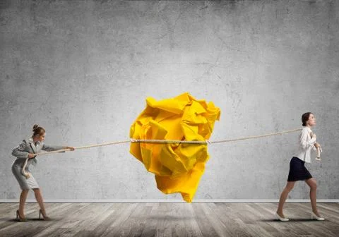 Two women pulling with effort big crumpled ball of paper as creativity sign Stock Photos