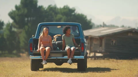 Two Women Riding In Back Of Pick Up Truck As Friends Arrive At Countryside Cabin Stock Footage 237413555