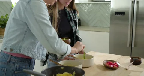 Two women scooping paste from wooden bowl on island, plating eggs into white Video stock 340069905