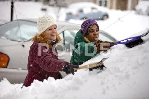 Two women scraping snow from windshield Stock Photos