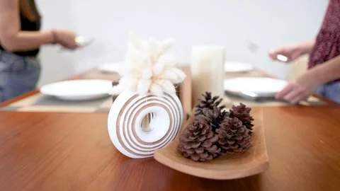 Two Women Setting a Minimalist Dining Table with Pine Cone Centerpiece Stock Footage 334983652