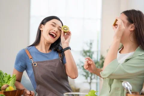 Two women share laughter while preparing food in a bright kitchen during th.. Stock Photos