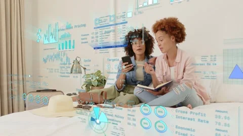 Two women sitting on bed, picking up phone comparing planner, planning trip Stock Footage 333485690