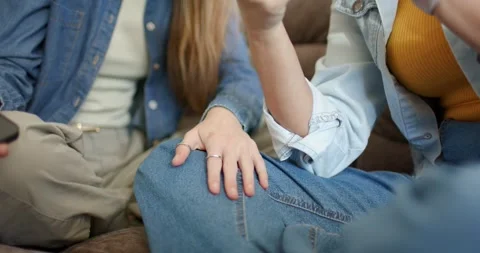 Two women sitting on sofa in denim, one gesturing, placing hand on other's knee Video stock 344948569