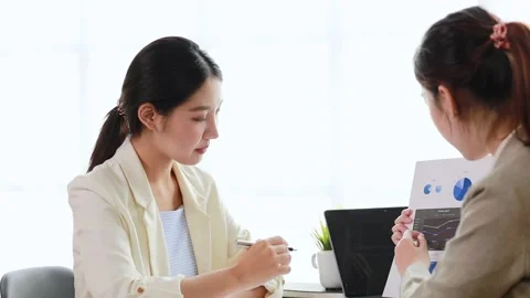 Two women sitting through white papers and talking Stock Footage 217513403