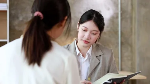 Two women sitting through white papers and talking Stock Footage 217514219