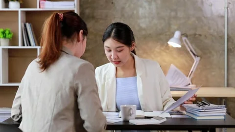 Two women sitting through white papers and talking Stock Footage 217514930