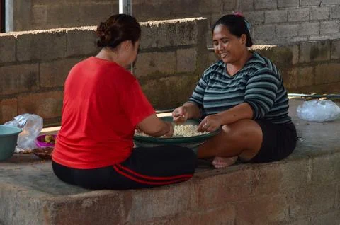 Two women smiling while peeling peanuts on a tray 스톡 사진