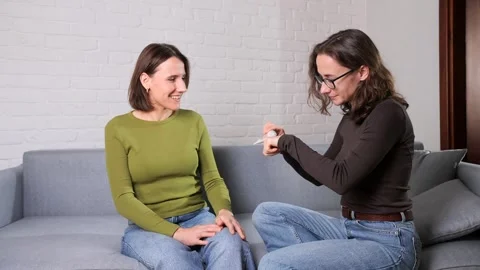 Two women on a sofa testing and discussing a new cosmetic cream, sharing Stock Footage 321262230