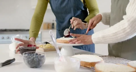 Two women stacking, scooping compote and spreading onto cake on stand, Stock Footage 346614101
