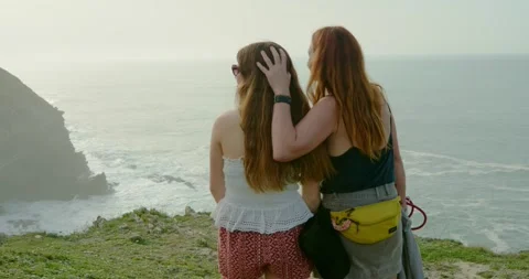 Two women stand side by side, embracing as they gaze out over the vast horizon. Stock Footage 334173546
