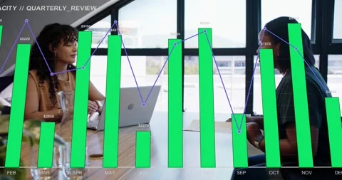 Two women at table, left operating laptop starting bars and trend line showing Stock Footage 332401572
