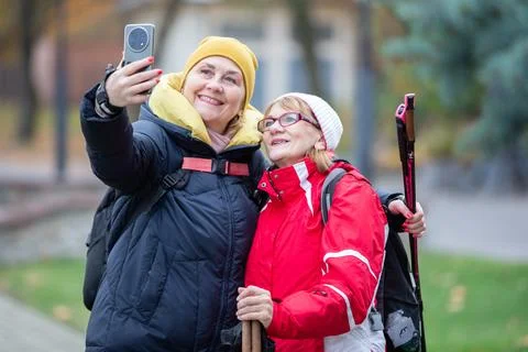 Two women take a selfie while walking in a park during autumn, wearing warm 库存照片