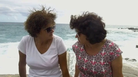 Two women talking while sitting in harbour by sea Stock Footage 84451643