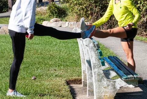 Two women using bench to stretch hamstrings in park Stock Photos