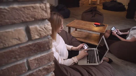 Two women using modern device sit in a bean bag chair 61336664