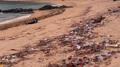Two women using a smartphone on a polluted tropical beach 動画素材 346336578
