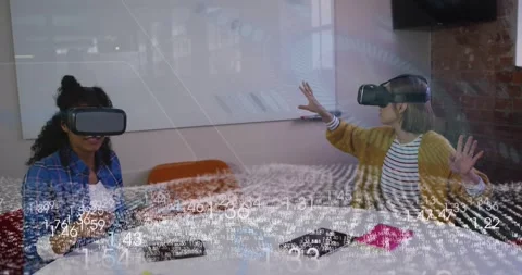 Two women in VR at table, data overlay appearing, one gesturing, other using Stock Footage 321099769