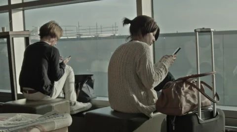 Two women waiting for flights using smartphones at the Gatwick Airport, London Stock Footage 40025095
