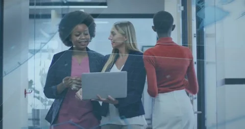 Two women walking corridor while scrolling laptop discussing business charts via Stock Footage 334178696
