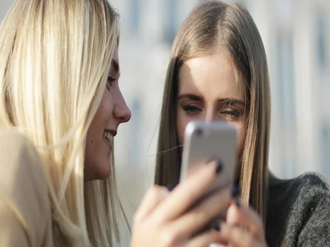 Two women watching at the screen of smartphone together outdoor. Stock Footage 80475594