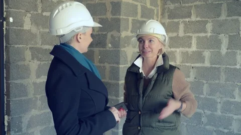 Two women in white helmets talking indoors with rough trim Stock Footage 122084486