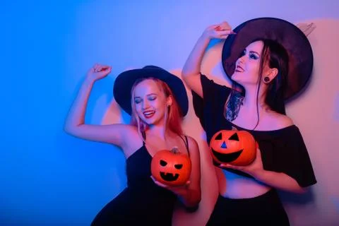 Two women witches hold pumpkins in their hands and dance. Women in neon light Stock Photos