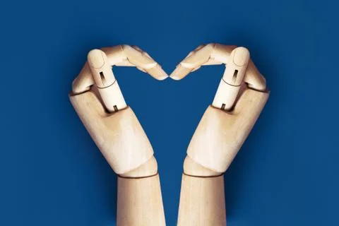 Two wooden hands folded in the shape of a heart on blue background Stock Photos