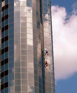 Two workers are cleaning the windows of a tall building while hanging from ro Stock Photos