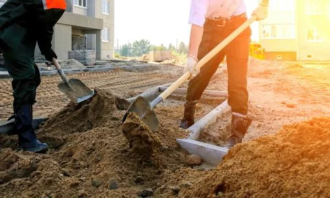 Two workers are digging and moving dirt at a construction site in a residenti Stock Photos