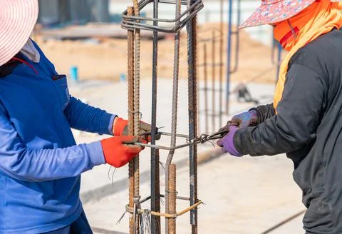 Two workers are tying wire to rebar to pour concrete poles. Stock Photos