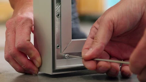 Two workers assemble a metal frame.Allen screws are screwed into the frame with Stock Footage 163078601