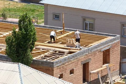 Two workers build roof frame on brick structure Stock Photos