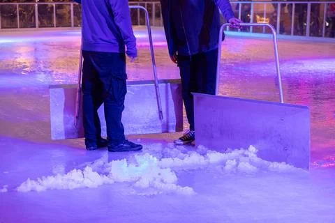 Two workers clean the ice surface with large metal scrapers at an outdoor rink Stock Photos