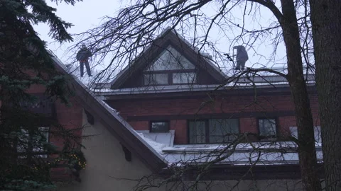 Two workers clearing snow with a shovels on a roof buiding Vidéo 263208399