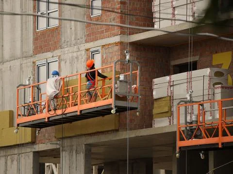 Two workers in a construction basket insulate the glassy wall of a multi-storey Stock Photos