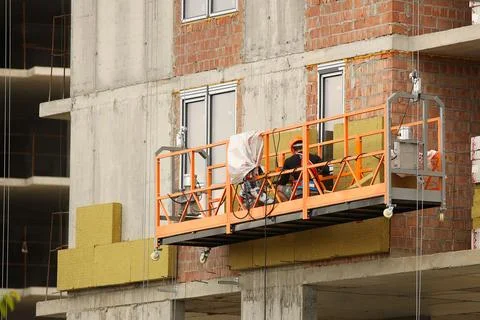 Two workers in a construction basket insulate the glassy wall of a multi-st.. Stock Photos