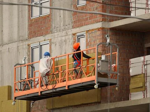 Two workers in a construction basket insulate the glassy wall of a multi-st.. Stock Photos