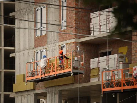 Two workers in a construction basket insulate the glassy wall of a multi-st.. Stock Photos