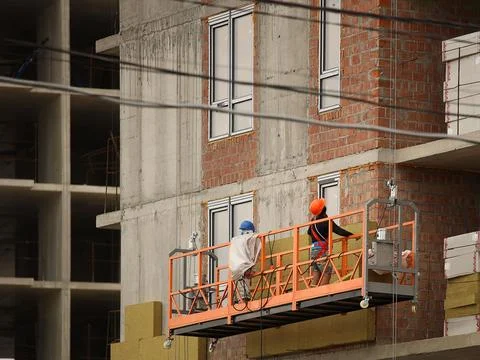 Two workers in a construction basket insulate the glassy wall of a multi-st.. Stock Photos