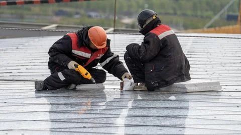 Two workers in construction winter clothes on the glass roof of a high-rise Stock Photos