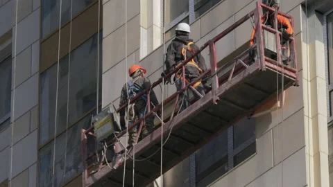 Two workers in a cradle rise along a high-rise building under construction Stock Footage 168582022