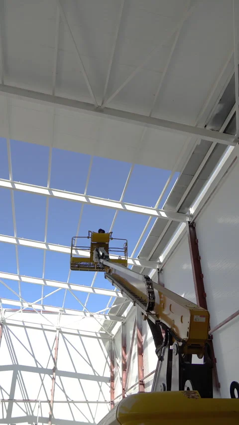 Two workers guiding sandwich panel onto hangar roof under construction, Almaty Stock Footage 335795719