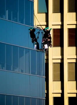 Two workers hanging from cables outside high rise building Foto stock